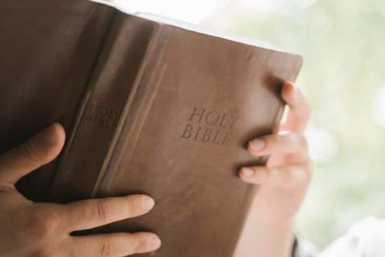 A person holding open a brown leather Bible as they read